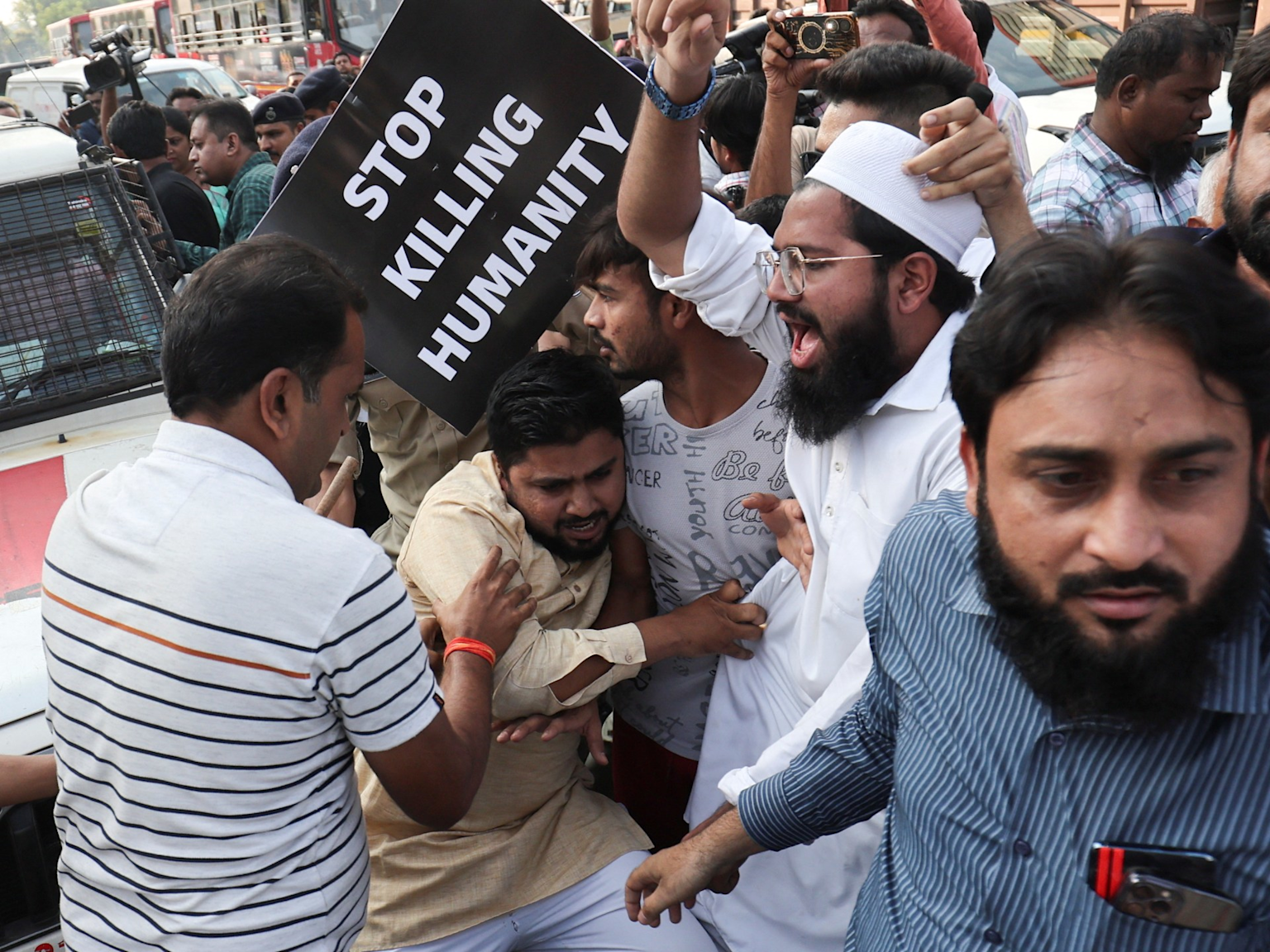 A group of people are protesting, with a prominent sign reading 'STOP KILLING HUMANITY'.